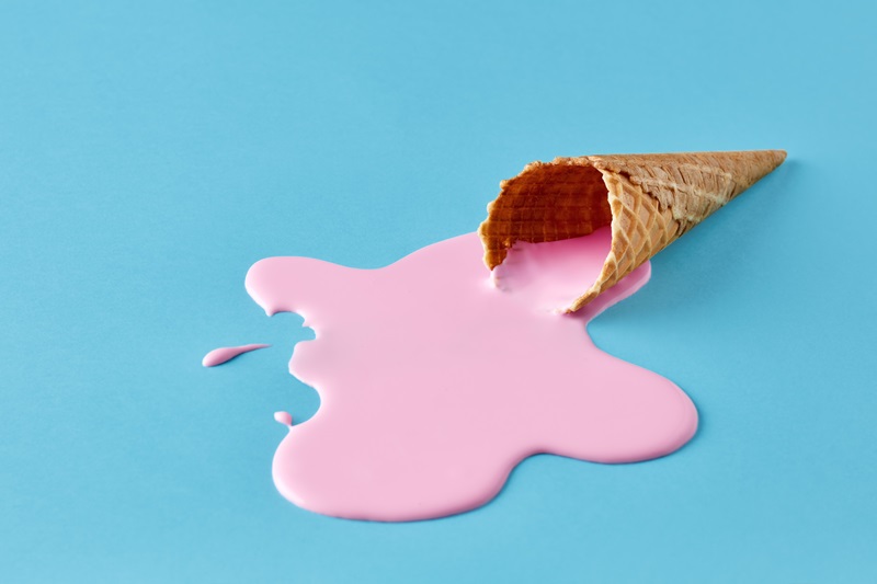 Pink ice cream melting and spilling from the waffle cone on pastel blue background. Minimalistic summer food concept.