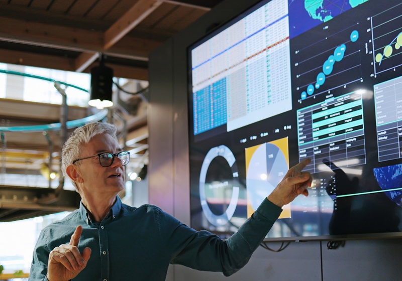 Stock image of a mature man conducting a seminar / lecture with the aid of a large screen. The screen is displaying graphs
