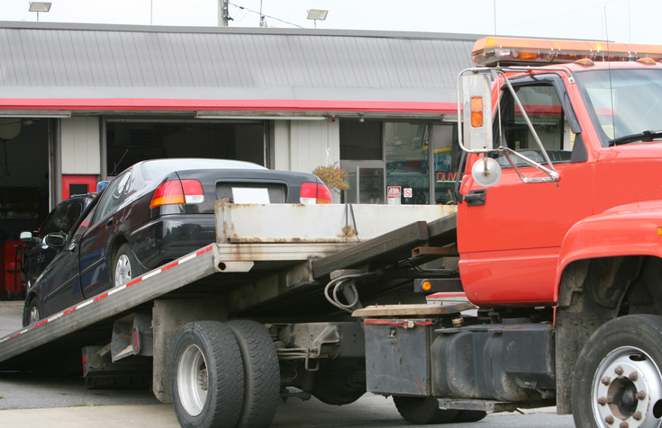 Black car on a red flat bed tow truck alternate text for this image