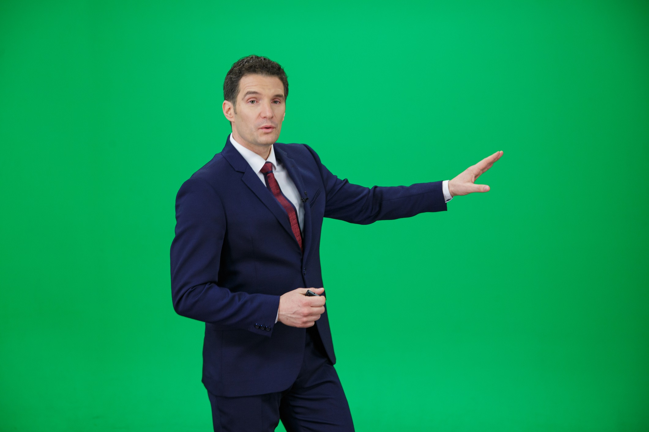 Caucasian weather man in front of a green background with small remote in his other hand.