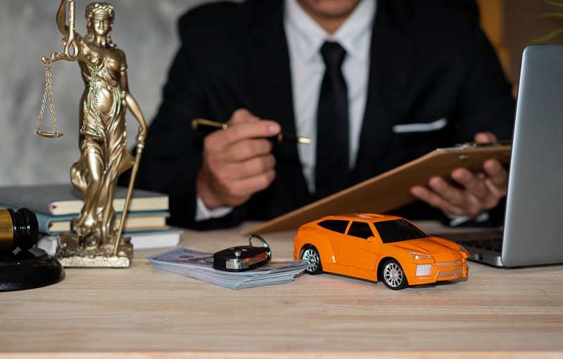 Small cars, keys and scales. Goddess of justice with hammer, money and laptop, and businessman holding a pen to sign a contract under car title approval concept.