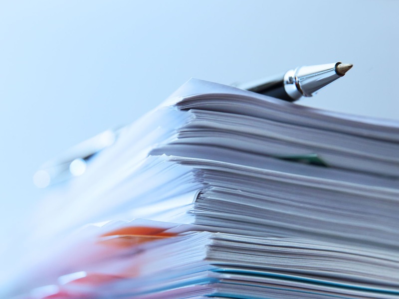 A stack of documents with a pen resting on top