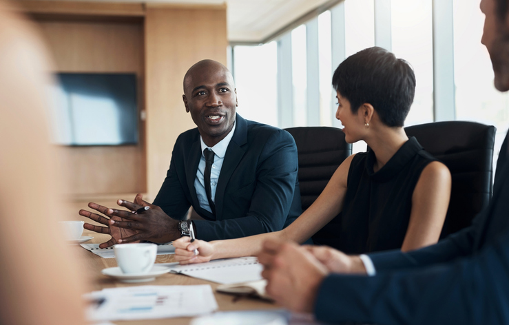 Business meeting, speaking and black man with discussion, planning and corporate proposal, staff update and leadership. Professional people in conference room talking, listening and career strategy alternate text for this image