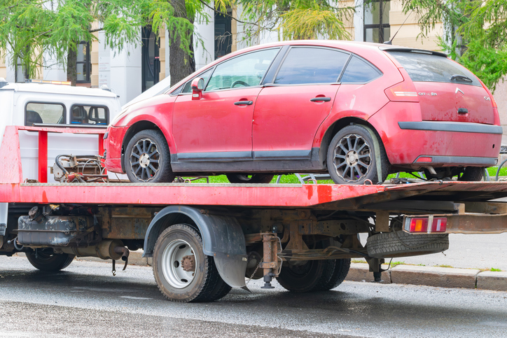 Red car loaded onto a tow truck. Towing cars violating parking rules. alternate text for this image