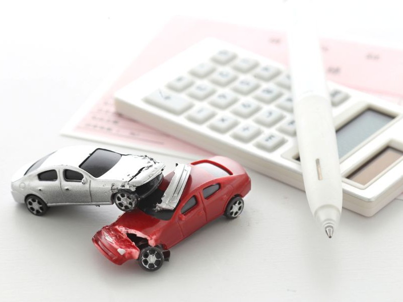 Toy cars crashing in front of calculator and pen to calculate the insurance costs