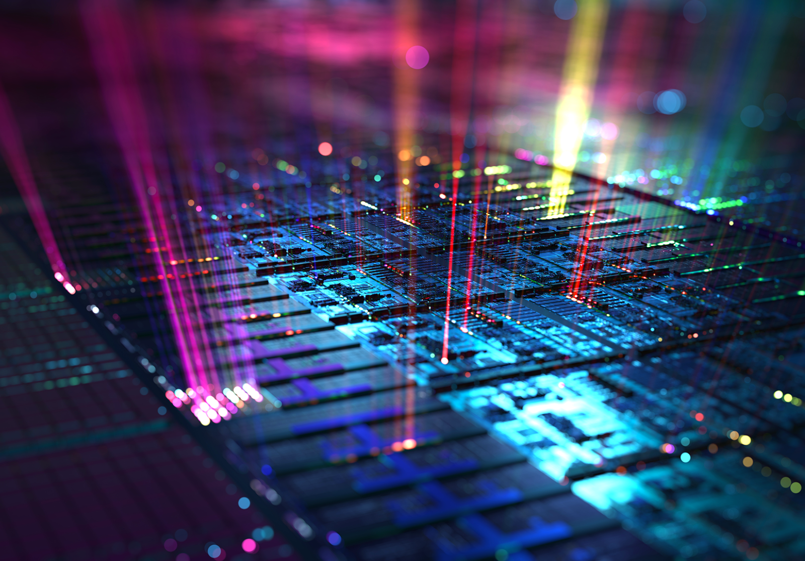 Colorful close-up of a computer microchip illuminated by vibrant beams of pink, yellow, blue, and green light, symbolizing data transmission or digital processing.