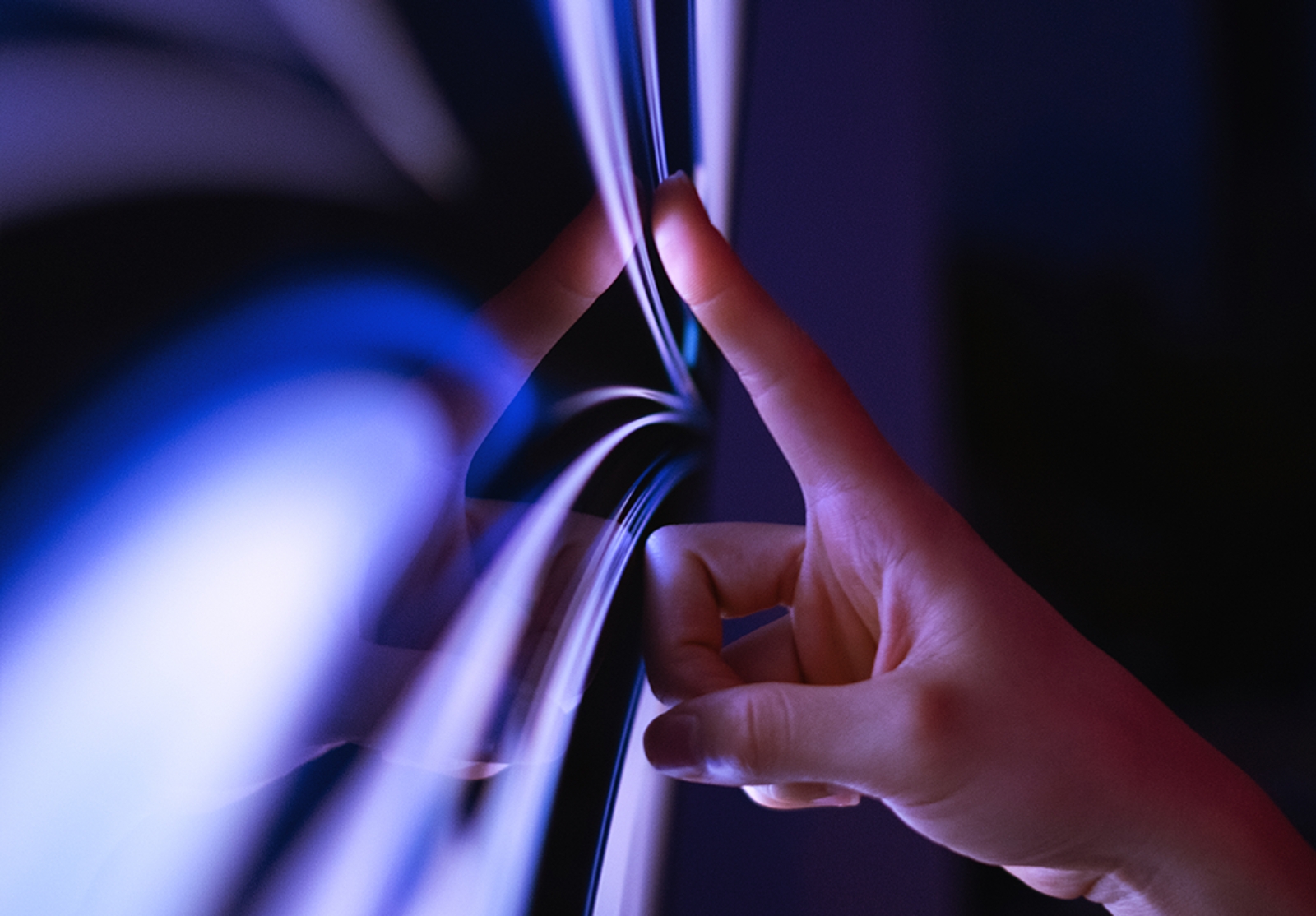 Finger touching a reflective surface, lit with blue and purple tones, suggesting a futuristic interface.