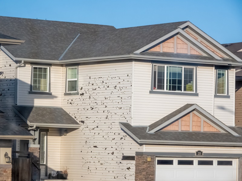 Calgary, Alberta, Canada. Apr 25, 2025. A multi-story house with light-colored siding showing signs of hail damage or wear seen on a sunny day.
