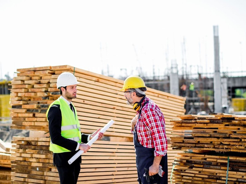 Construction site manager and worker dealing with blueprints and projects.