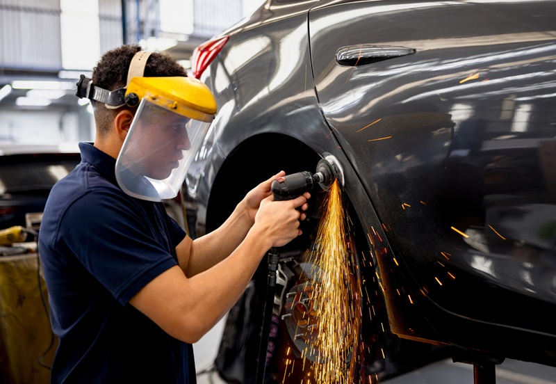 Mechanic grinding a car while working at an auto repair shop and using protective workwear