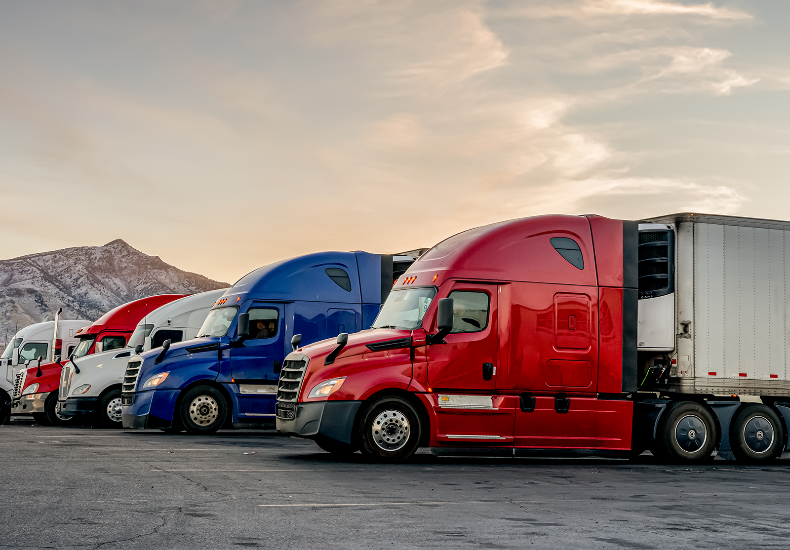 Colorful semi-trailer trucks parked at sunset with mountains in the background.
