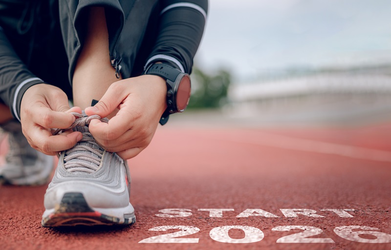 Close-up of hands tying shoelaces on a running track marked START 2026, representing preparation, focus, and readiness for new goals and fitness resolutions in the upcoming year.