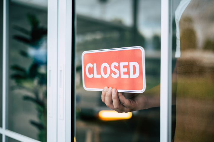 A retail store owner in a coffee shop is seen turning the closed sign alternate text for this image