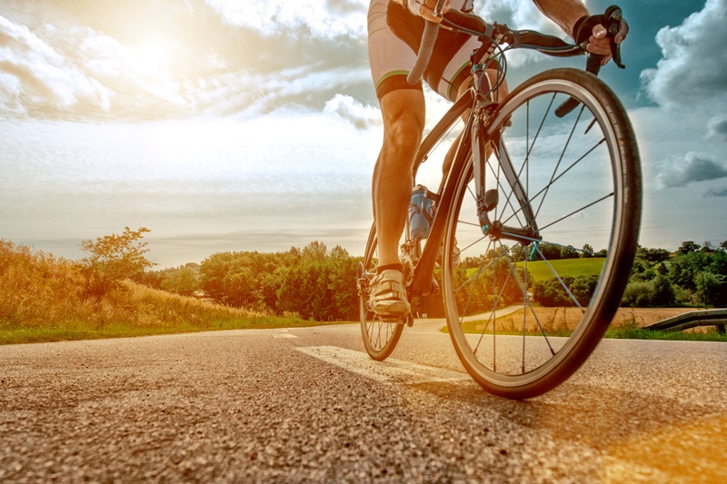 Close up of a athlete who rides his bike up a steep hill. The sun shines as his feet hits the pedals and he drives the bicycle forward.