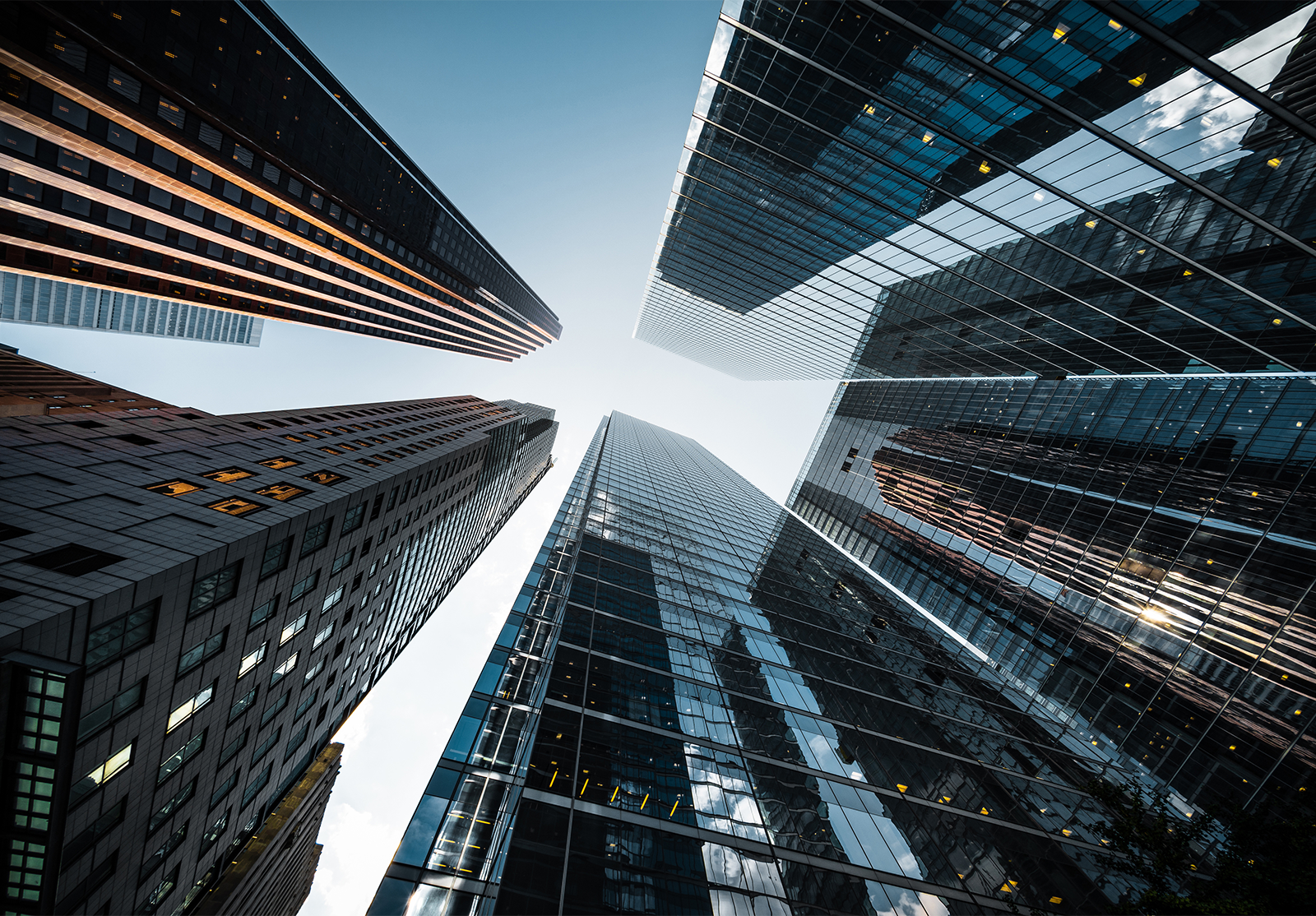 Upward view of modern skyscrapers with reflective glass facades converging toward a clear blue sky, emphasizing height and urban architecture.