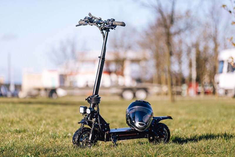 Photo of one black electric puch scooter outdoors. Kickscooter on the green grass near the building. Protective helmet on the deck. Ecological transport concept photography, lifestyle photo