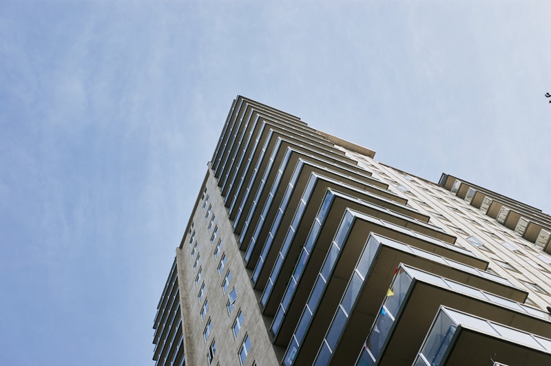 Low-angle view of a tall brick apartment building framed by green trees under a clear sky in Saskatchewan, Canada.