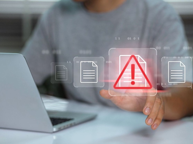 Businessman using laptop with spam warning symbol displayed