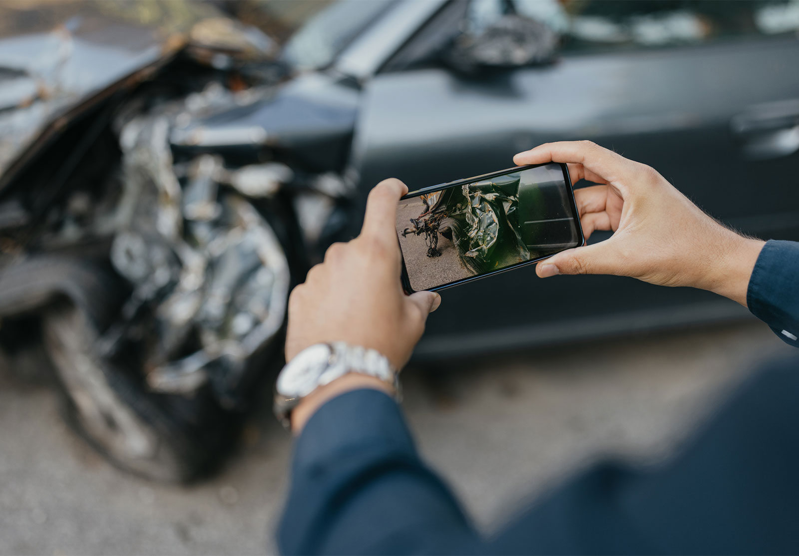 Person photographing the crumpled front end of a damaged car with a smartphone after a collision.