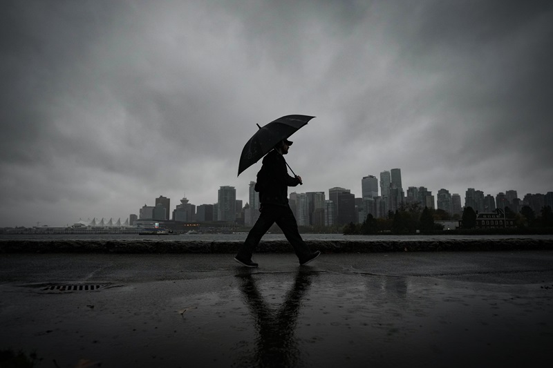 A man uses an umbrella to shield himself from the rain while walking on the Stanley Park seawall across the water from downtown Vancouver on Saturday, Oct. 19, 2024. THE CANADIAN PRESS/Darryl Dyck