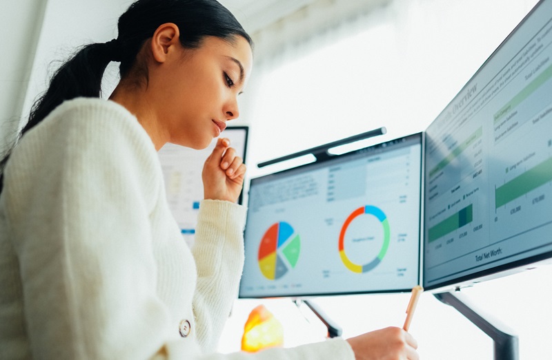 Woman working at home looking at charts on her computer monitor