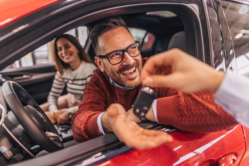 A couple sitting in a car, receiving the keys from a car rental agent