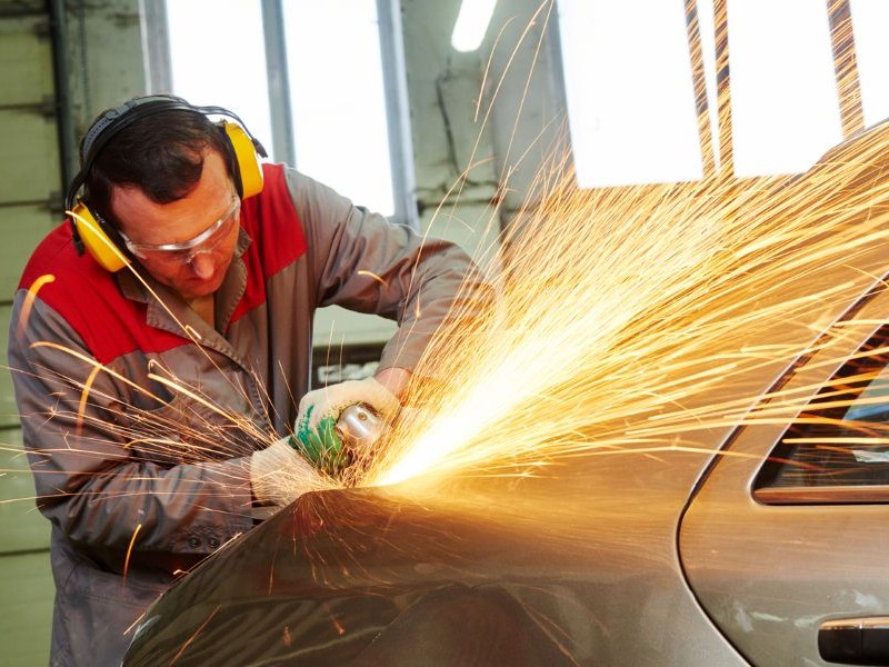 Auto body tech using a grinder on a car